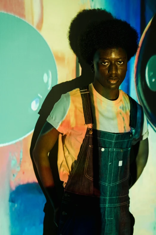 a man standing in front of a painting, an album cover, trending on pexels, afrofuturism, wearing overalls, washed out colors, photo from a promo shoot, black man with afro hair