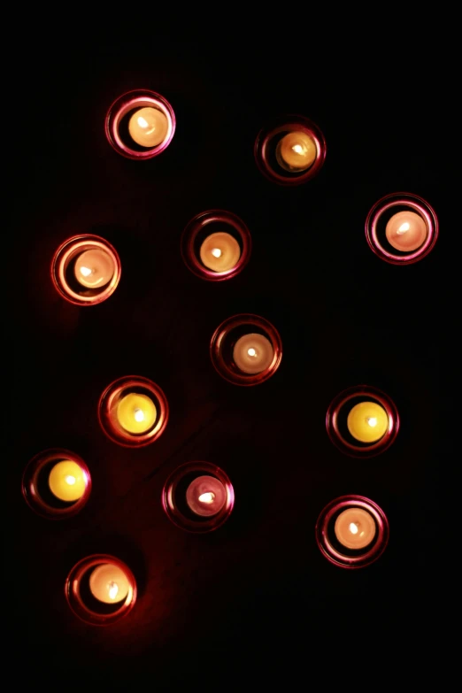 a group of lit candles in a dark room, circles, soft lighting from above, laura watson, full frame image