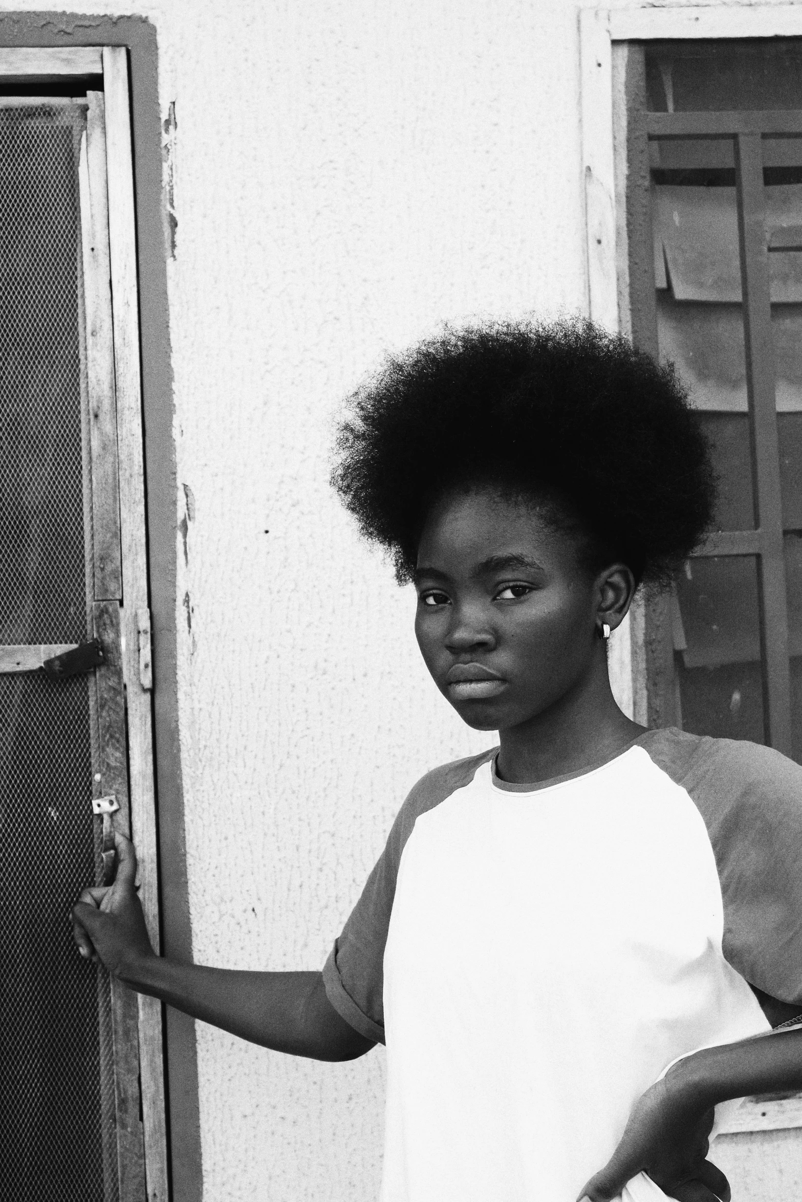 a black and white photo of a woman standing in front of a door, flickr, afrofuturism, portrait of a young teenage girl, whitebangsblackhair, an aesthetic!