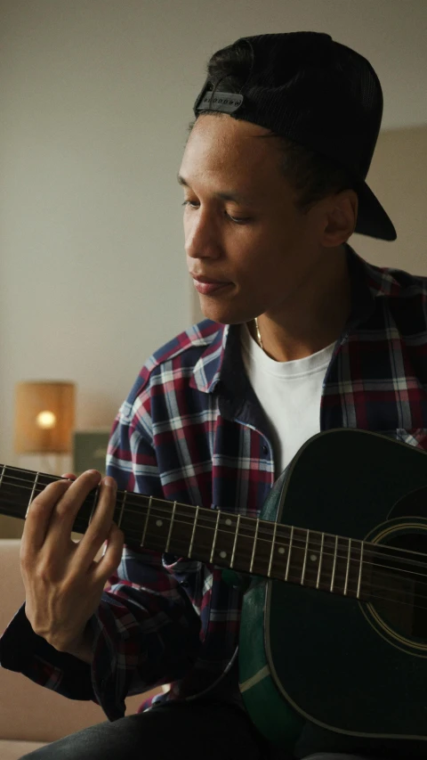 a man sitting on a couch playing a guitar, by Jacob Toorenvliet, pexels, realism, portrait of tom holland, tom morello, profile image, ashteroth