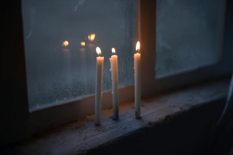 a group of white candles sitting on top of a window sill, inspired by Elsa Bleda, unsplash, dark damp atmosphere, mikko lagerstedt, battered, winter setting