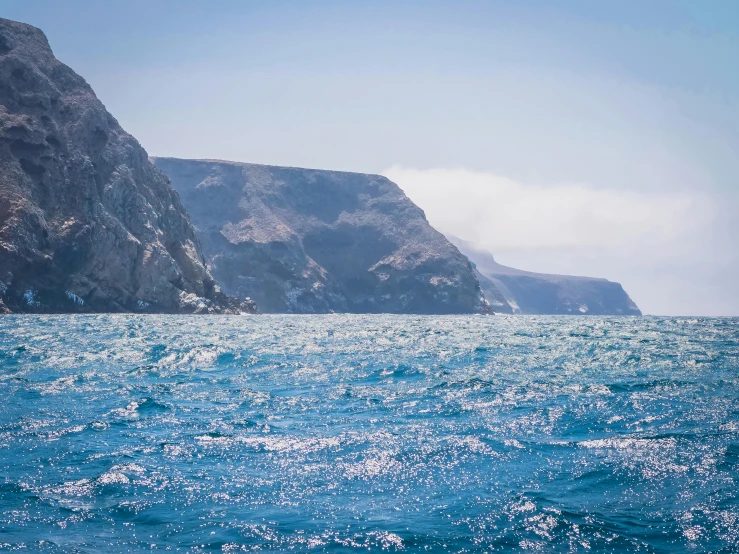 a body of water with a mountain in the background, a photo, coastal cliffs, offshore winds, light blue water, thalassophobia