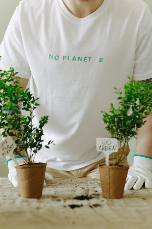 a man sitting at a table with three potted plants, pexels contest winner, plasticien, lab coat and tee shirt, our planet, labels, no greenery