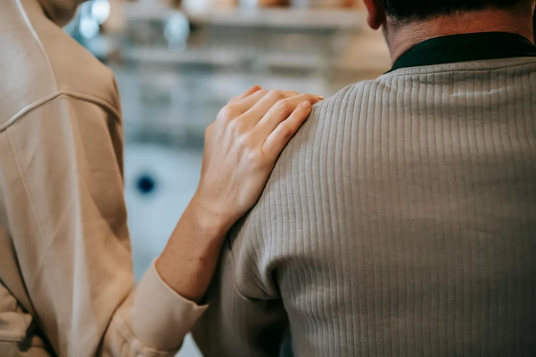 a man and a woman standing next to each other, trending on pexels, showing her shoulder from back, comforting, sitting down, professional image