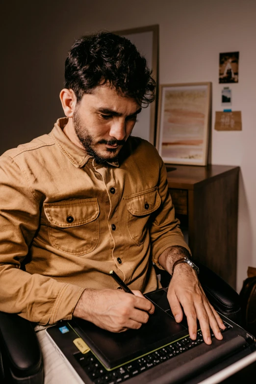 a man sitting in a chair working on a laptop, inspired by Germán Londoño, trending on pexels, brown jacket, signing a bill, caramel. rugged, portrait of danny gonzalez