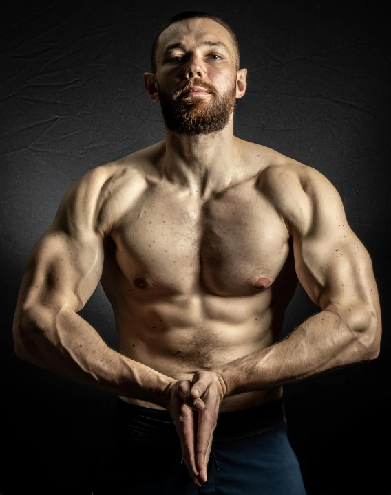 a shirtless man standing in front of a black background, a colorized photo, flexing large muscles, lgbt, non binary model, bearded and built