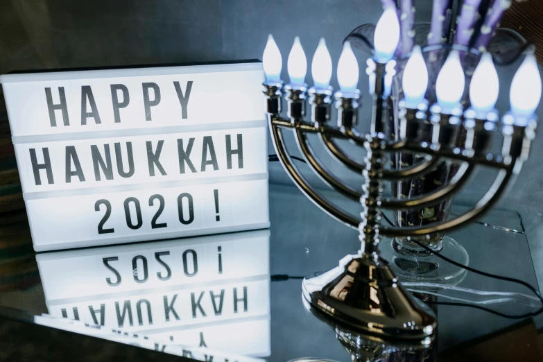 a menorah sitting on top of a table next to a sign that says happy hanukkah 2020, by Niko Henrichon, trending on unsplash, hurufiyya, light box, youtube thumbnail, frontal shot, dark. no text