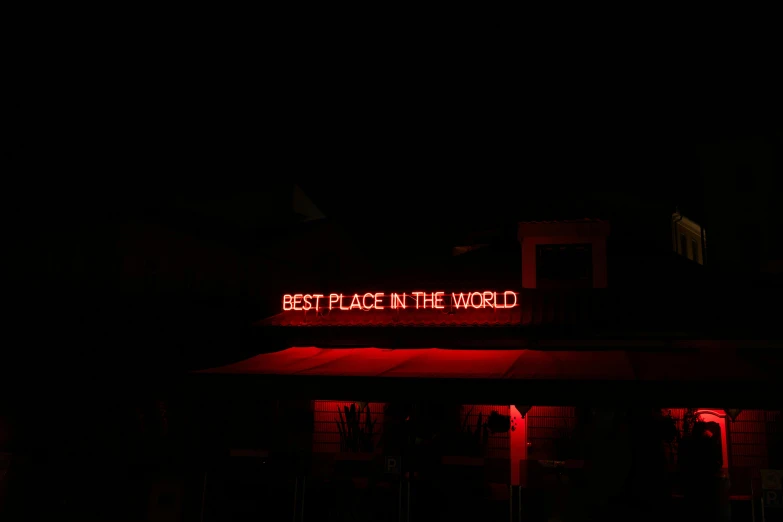 a building with a neon sign that says best place in the world, pexels contest winner, dark red, alternative world, near the beach, rex orange county