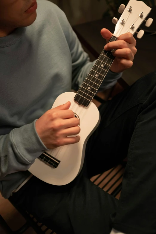 a man sitting on the floor playing a white ukulele, matte finish, hand model, neck zoomed in, highly upvoted