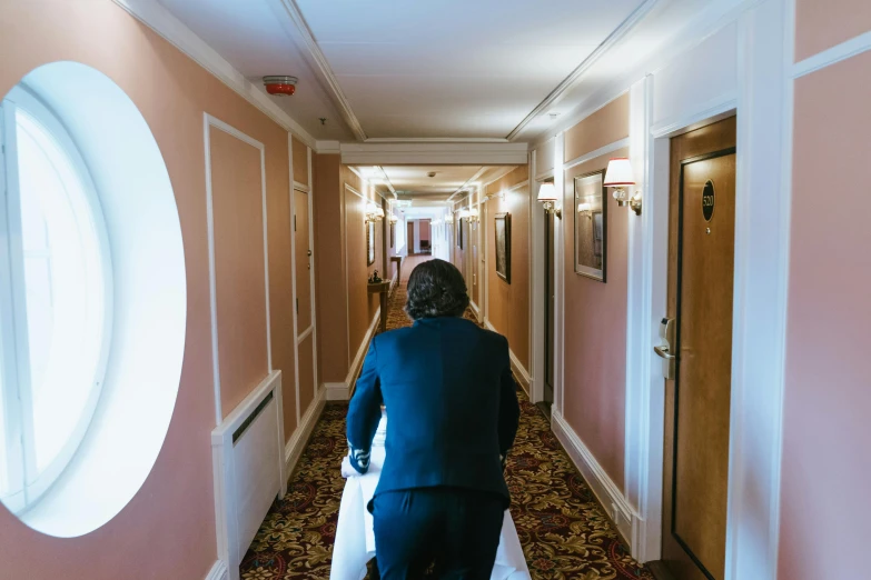 a woman is walking down a long hallway, an album cover, by Julia Pishtar, unsplash, happening, groom, hotel room, in the style wes anderson, thumbnail