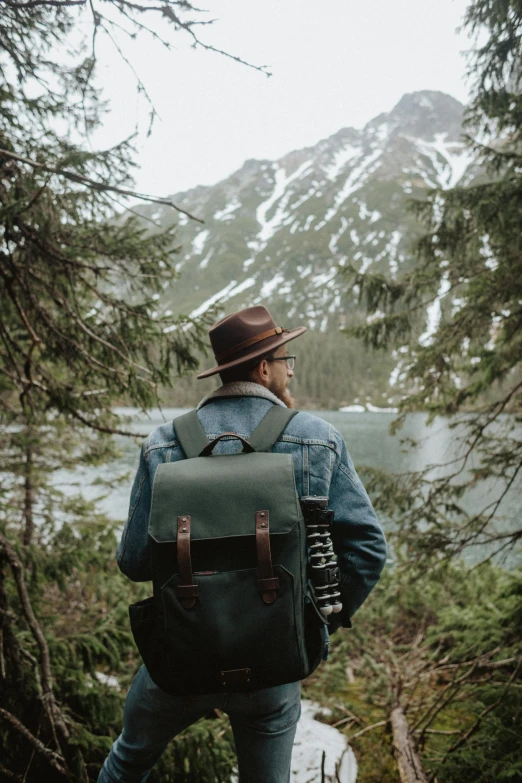 a man standing in the woods with a backpack, a picture, by Jessie Algie, trending on unsplash, alaska, vintage style, overlooking the ocean, cinematic outfit photo