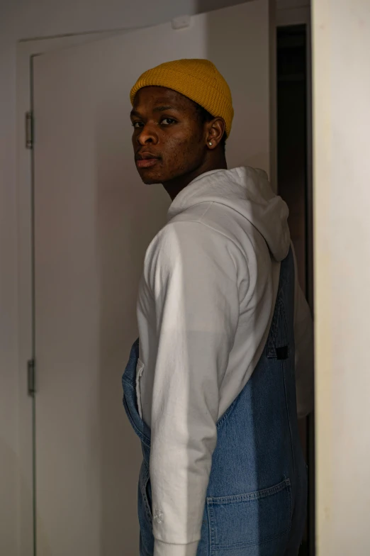 a man with a yellow hat standing in a doorway, unsplash, realism, young thug, wearing overalls, in white turtleneck shirt, ( ( theatrical ) )