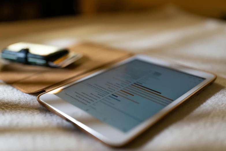 a tablet computer sitting on top of a bed, by Carey Morris, charts, teaser, brown, sharp focus »