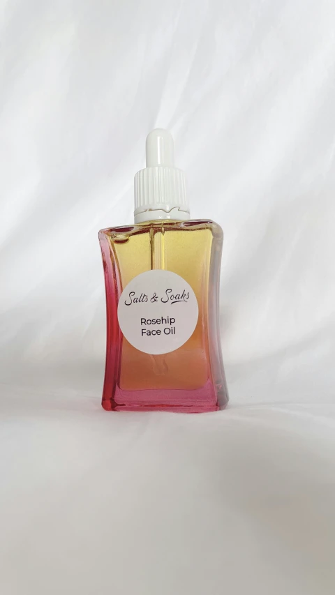 a bottle of liquid sitting on top of a bed, by Dean Ellis, purism, pink and gold, sweet almost oil, vanilla, soft lightening