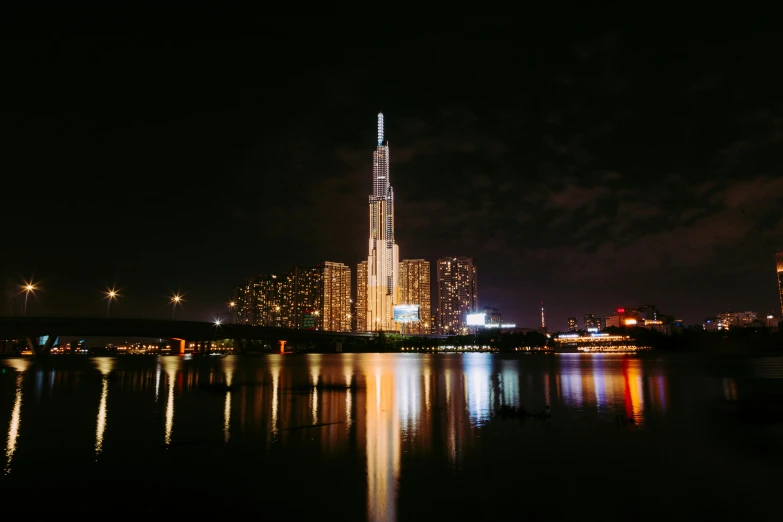 a view of a city at night from across the water, an album cover, pexels contest winner, modernism, gigantic tower, vietnam, sharp high quality photo, medium height
