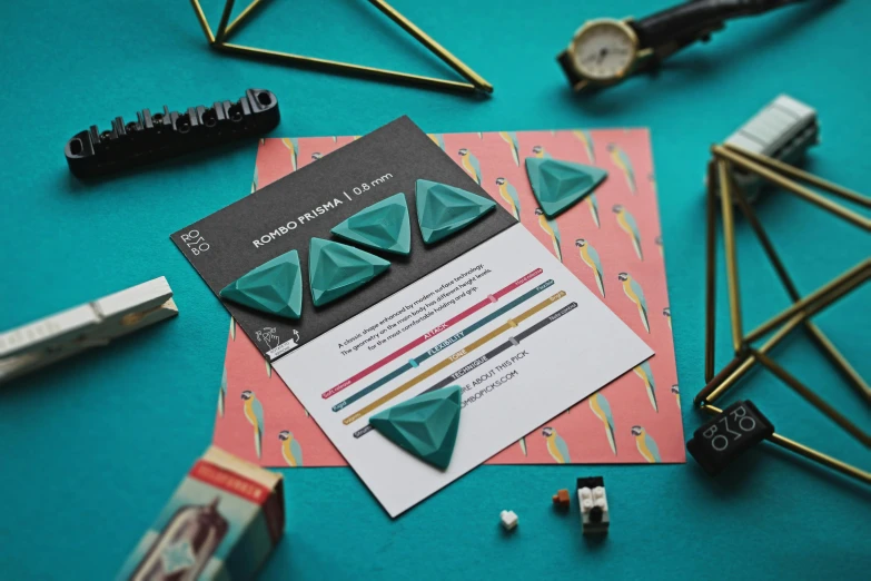 a close up of a business card on a table, by Emma Andijewska, op art, emerald earrings, origami, dark teal, instructions