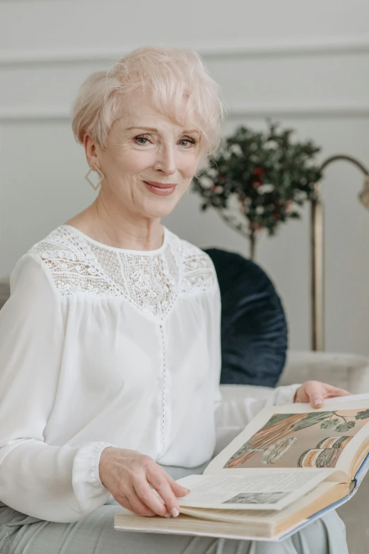 a woman sitting on a couch reading a book, a character portrait, inspired by Elsa Beskow, short white hair, portrait image, on a white table, colour photo