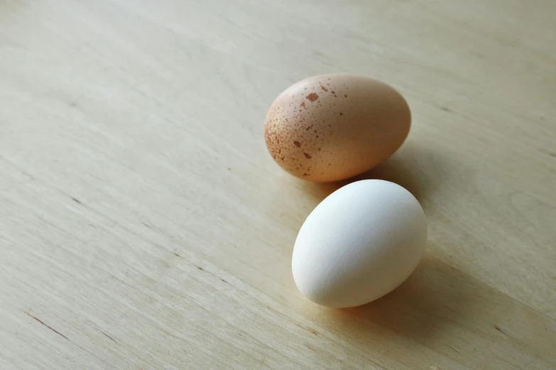 a couple of eggs sitting on top of a wooden table, by Sylvia Wishart, unsplash, pale-skinned, half and half, close-up product photo, agile