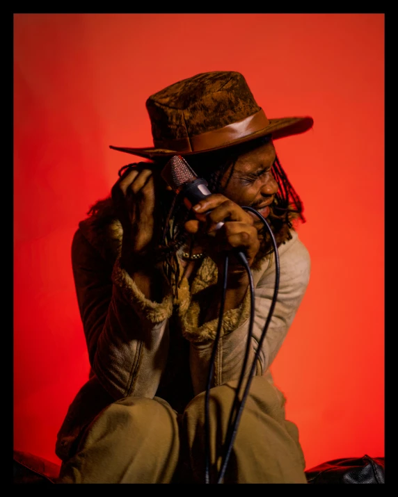 a man in a hat talking on a cell phone, an album cover, inspired by Candido Bido, unsplash, afrofuturism, dreads, red horns, shot in the photo studio, muted brown