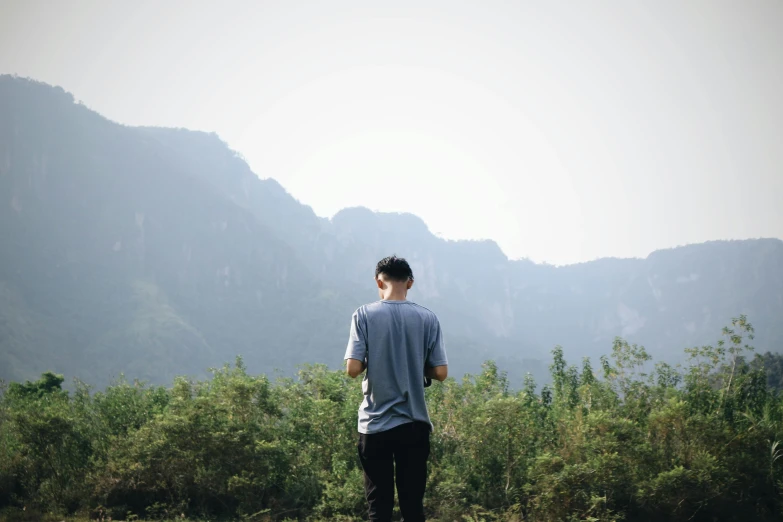 a man flying a kite on top of a lush green field, by Cheng Jiasui, pexels contest winner, standing in a grotto, wearing pants and a t-shirt, avatar image, distant thoughtful look