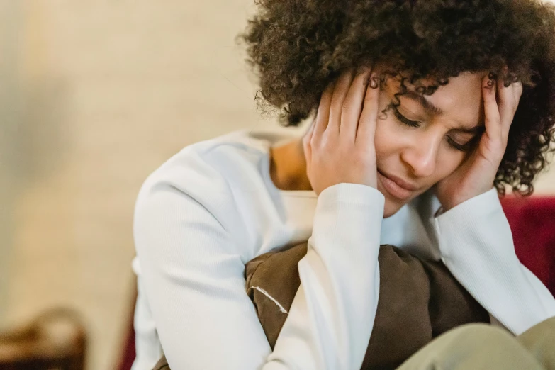 a woman sitting on a couch with her head in her hands, trending on pexels, renaissance, embracing, tinnitus, black young woman, two exhausted