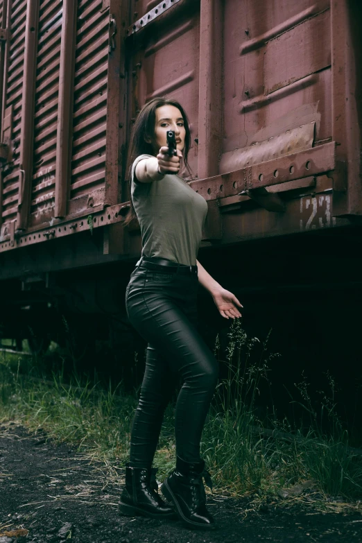 a woman posing in front of a train, by Adam Marczyński, pexels contest winner, dramatic wielding gun pose, better known as amouranth, leather clothing, action thriller