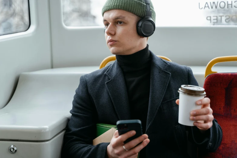 a man sitting on a bus holding a cup of coffee and a cell phone, an album cover, trending on pexels, gaming headset, wearing a turtleneck and jacket, avatar image, professional modeling