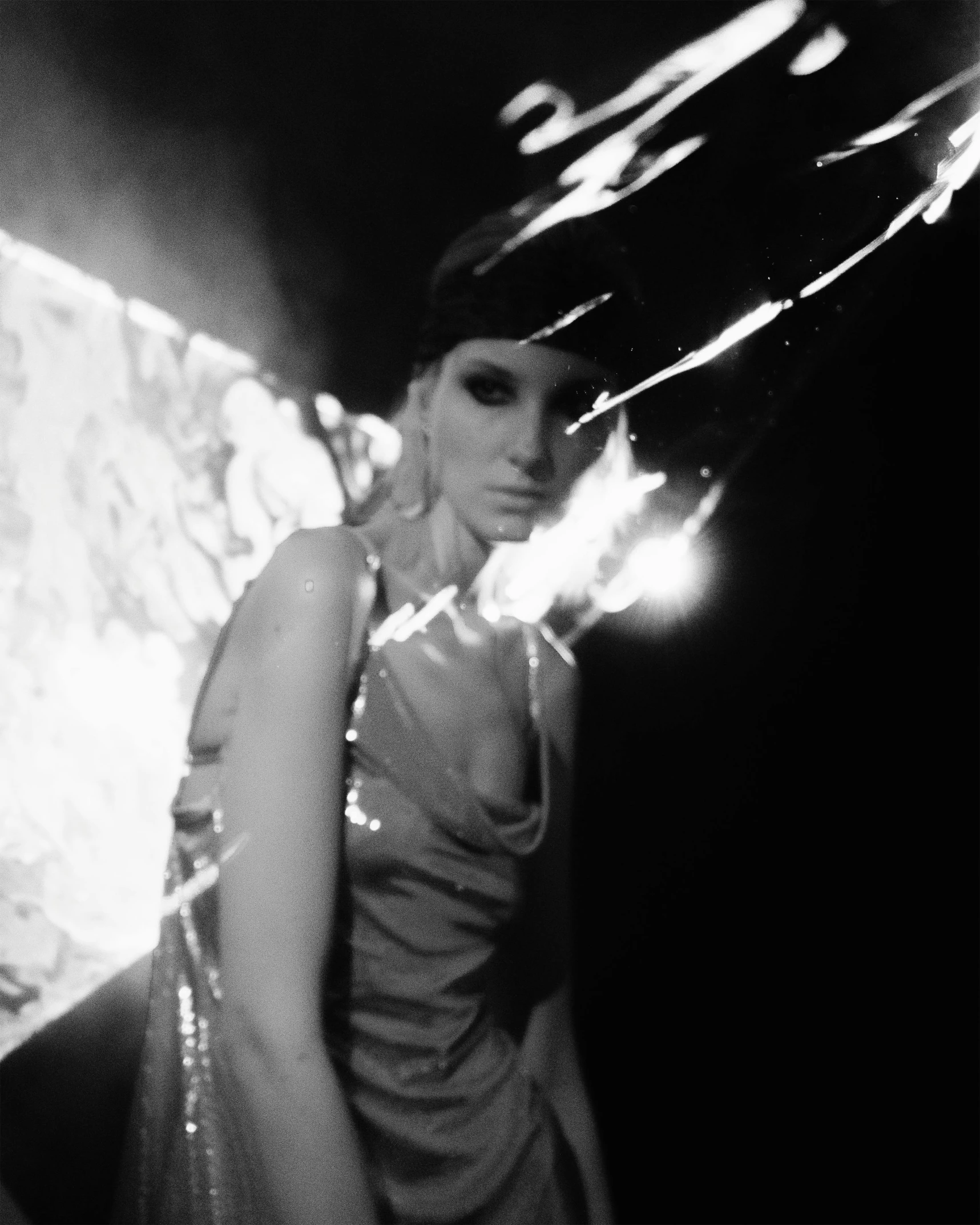 a black and white photo of a woman in a dress, inspired by Claude Cahun, video art, fire raining, with lots of glittering light, low quality photo, seventies cinestill