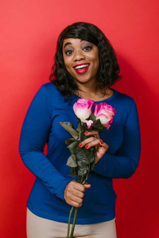 a woman holding a bouquet of flowers in front of a red wall, in a navy blue sweater, rodney matthew, comedic, promotional image