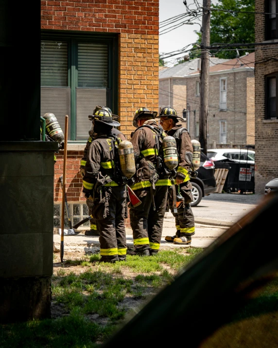 a group of firefighters standing in front of a building, by Andrew Domachowski, neighborhood outside window, background image, lgbtq, scorching heat