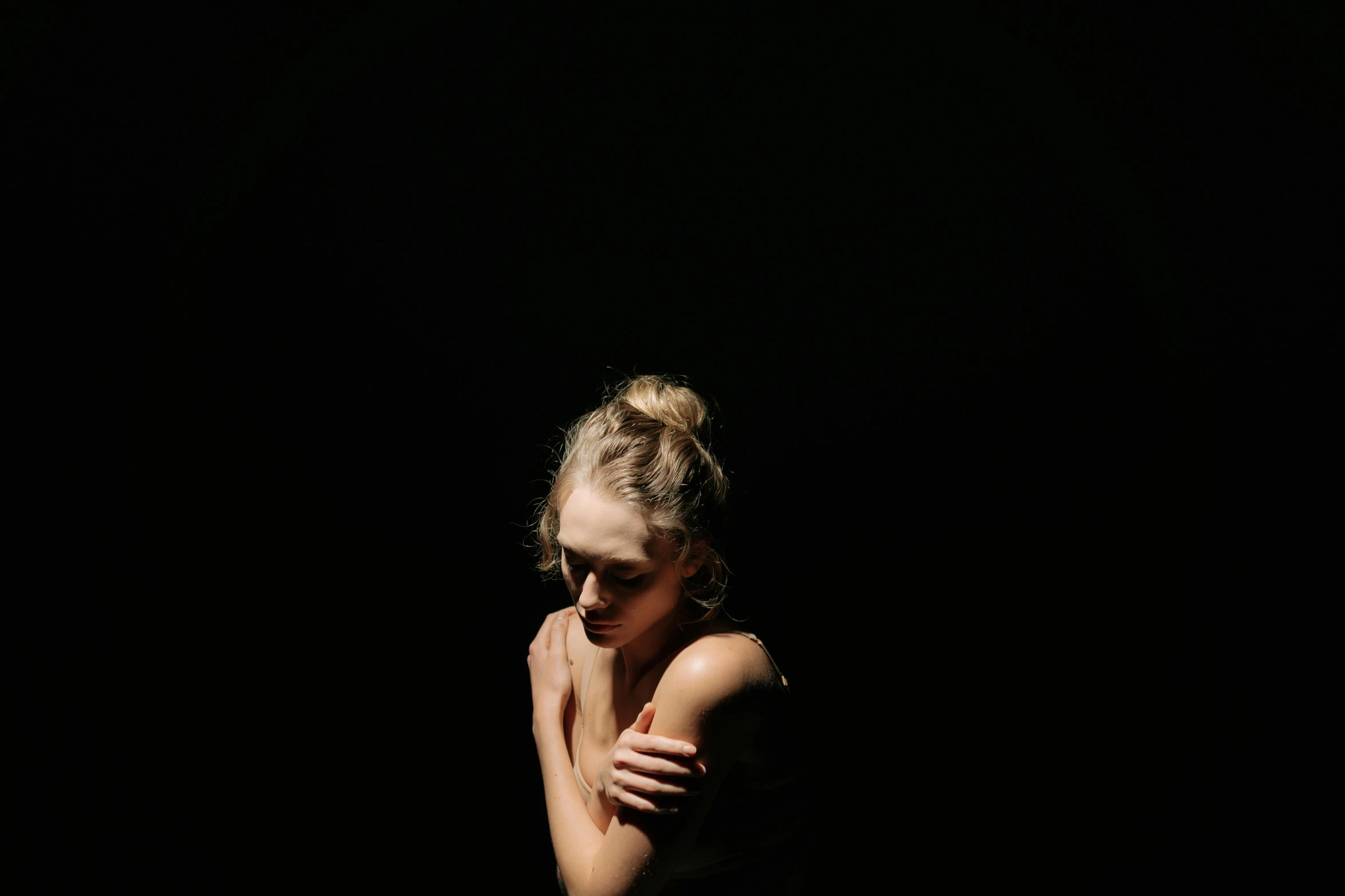 a woman standing in the dark with her hands on her chest, inspired by Elsa Bleda, unsplash, minimalism, portrait of annasophia robb, black background, sitting, sunlit