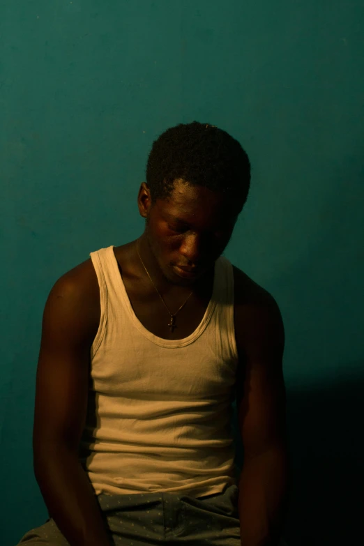 a man sitting in front of a blue wall, an album cover, pexels contest winner, dark brown skin, scene from a movie, timid and vulnerable expression, african