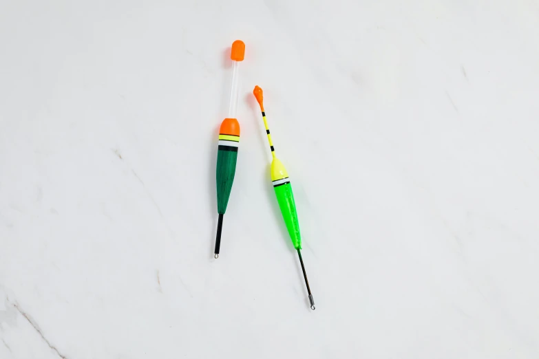 two toothbrushes sitting next to each other on a marble surface, by Nicolette Macnamara, fishing, green and orange theme, dipstick tail, miniature product photo