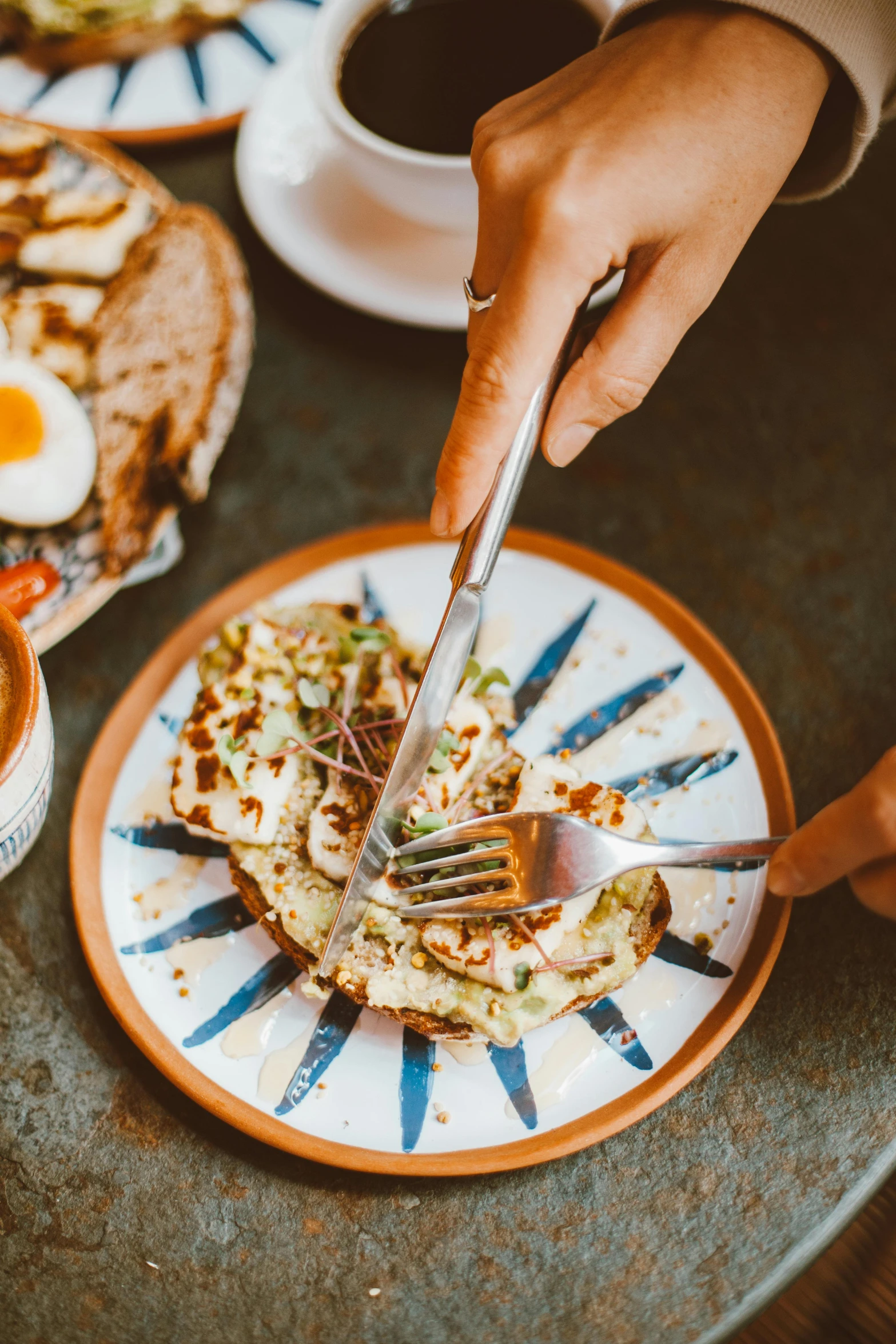 a table topped with plates of food next to a cup of coffee, by Julia Pishtar, using fork, eggs, hands on counter, toast