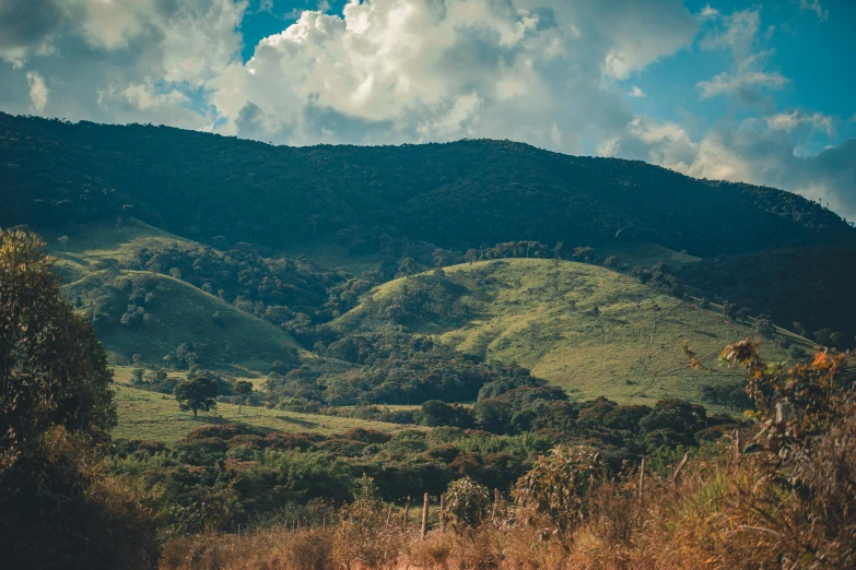 a person riding a motorcycle down a dirt road, an album cover, unsplash contest winner, sumatraism, distant town in valley and hills, colombian jungle, background image, grassy hills