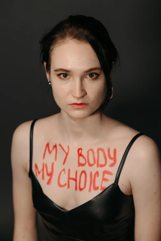 a woman with the words my body my choice painted on her chest, an album cover, inspired by Vanessa Beecroft, feminist art, carice van houten, teenage girl, lgbtq, horror ”