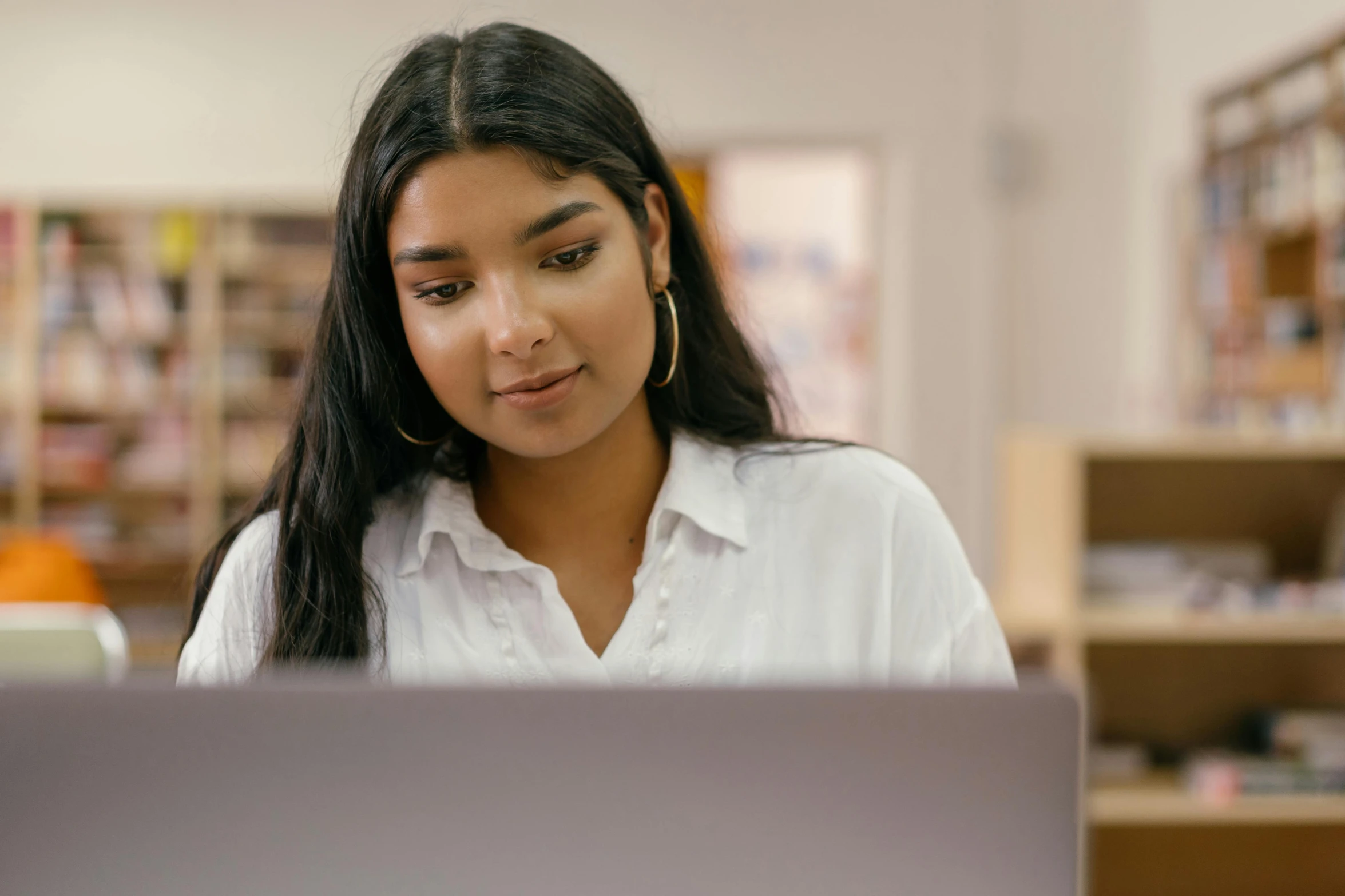 a woman sitting in front of a laptop computer, trending on pexels, academic art, indian girl with brown skin, librarian, looking her shoulder, performing