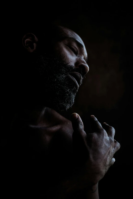 a man is praying in the dark, an album cover, inspired by Lee Jeffries, hyperrealism, small dark grey beard, man is with black skin, medium format. soft light, photography of albert watson