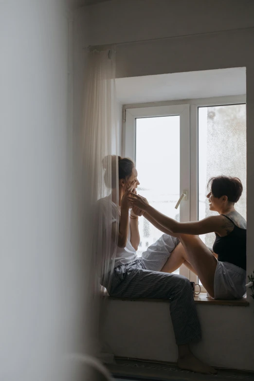 a couple of people sitting on a window sill, pexels contest winner, romanticism, lesbian kiss, in small room, reaching out to each other, springtime morning