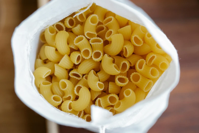 a bag of pasta sitting on top of a wooden table, a picture, curled slightly at the ends, getty images, close-up photo, jen atkin