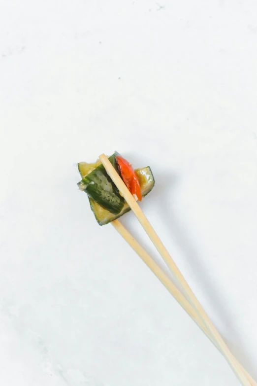 a pair of chopsticks with vegetables on them, zoomed out to show entire image, cucumber, square, dynamic angled shot