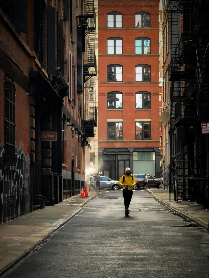 a person in a yellow jacket walking down a street, by David Palumbo, pexels contest winner, new york buildings, alleys, ignant, boston massachusetts