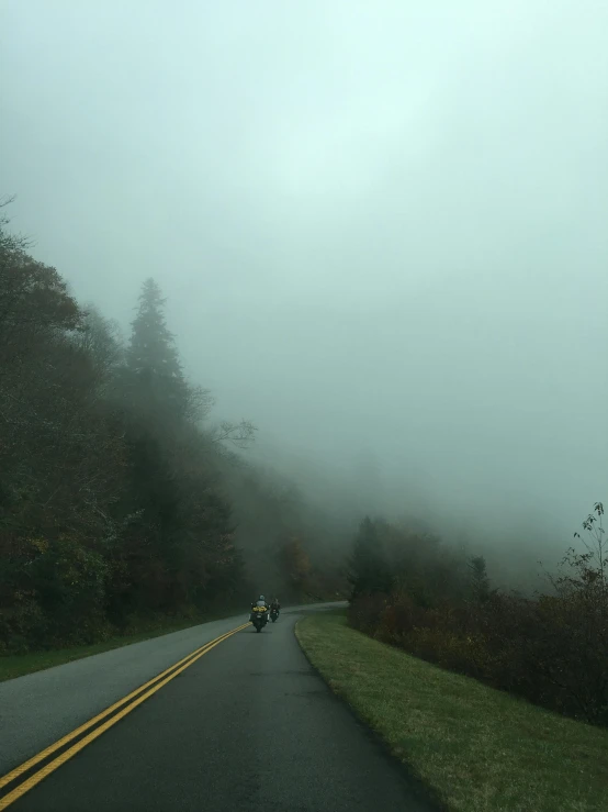 a person riding a motorcycle on a foggy road, noelle stevenson, aubrey powell, craggy mountains, overcast!!!