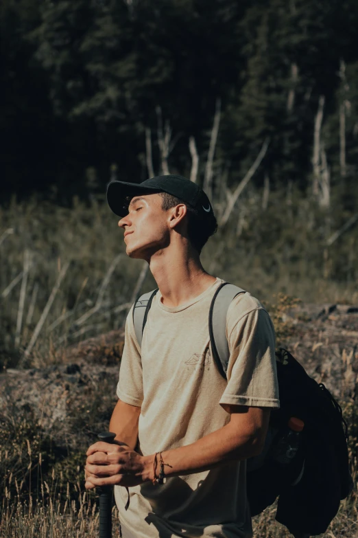 a man standing in a field with a backpack, unsplash contest winner, lean man with light tan skin, profile image, forested, wearing a baseball cap backwards