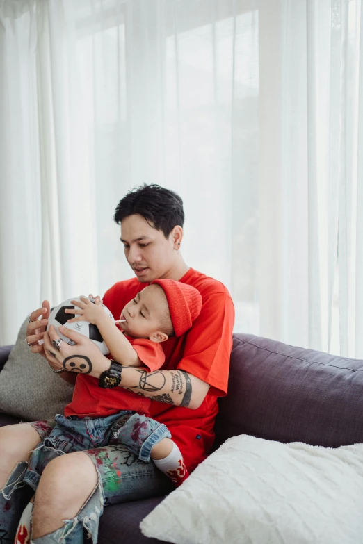 a man sitting on a couch holding a baby, a cartoon, by Basuki Abdullah, pexels contest winner, square, tattooed, ruan jia and brom, gif