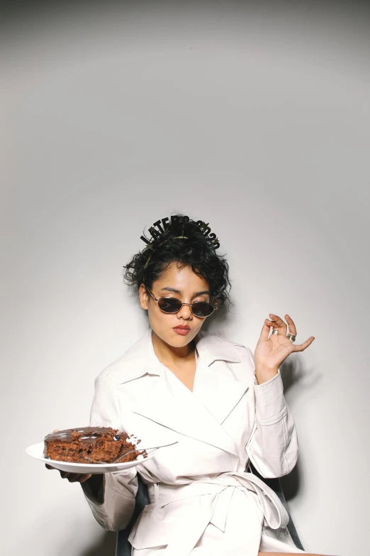 a woman sitting on a chair holding a plate of cake, an album cover, inspired by Pia Fries, trending on pexels, wearing sunglasses, mixed race, model standing pose, bun )