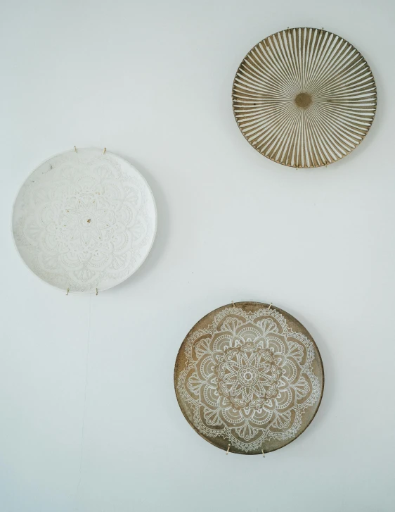 a number of plates on a wall near one another, an etching, by Felicity Charlton, trending on unsplash, arts and crafts movement, gradient white to gold, in a white boho style studio, made of intricate metal and wood, detailed product photo