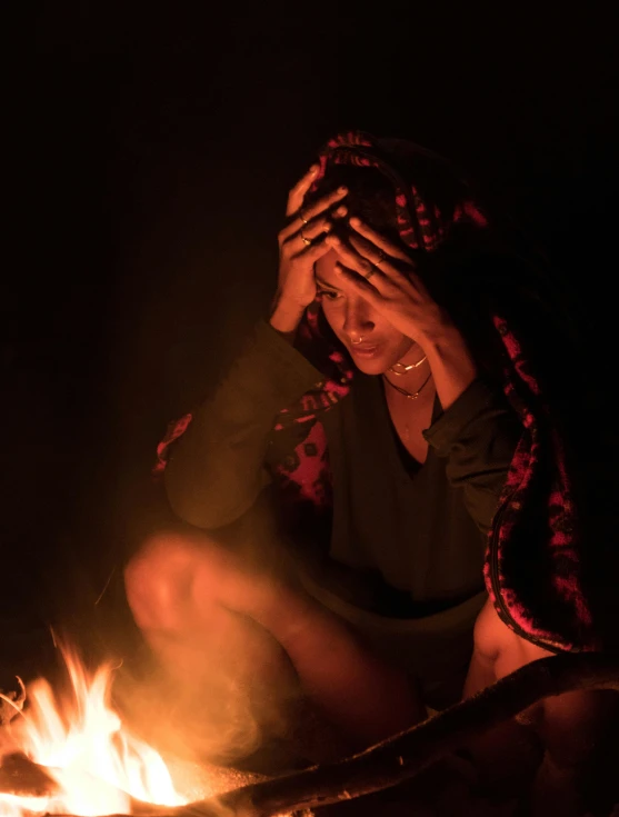 a woman sitting in front of a fire in the dark, by Jan Tengnagel, hurufiyya, unhappy, young himalayan woman, background image, camp