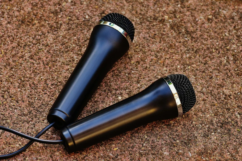 a pair of microphones laying on the ground, by Tom Carapic, pixabay, hurufiyya, black plastic, ultrarealistic, handheld, album