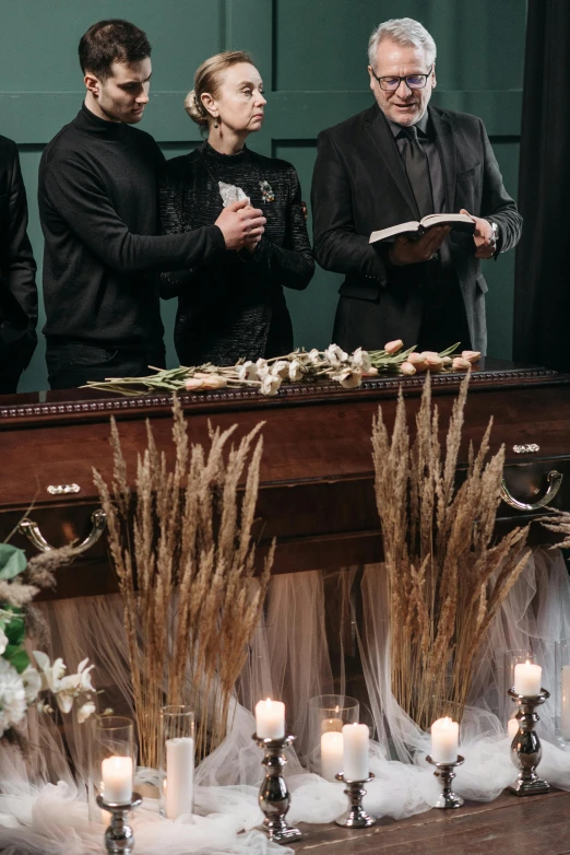 a group of people standing around a table with candles, casket, gothic aesthetic, flowers, high quality photo